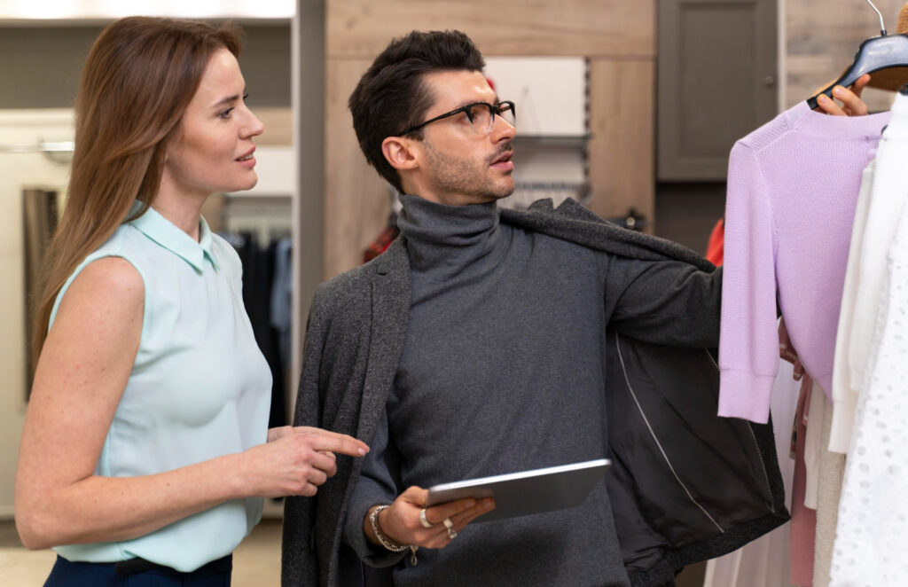 Cliente consultando una prenda en tienda con ayuda de una dependienta y una tablet, representando cómo la presencia online influye en la experiencia del cliente en tienda.
